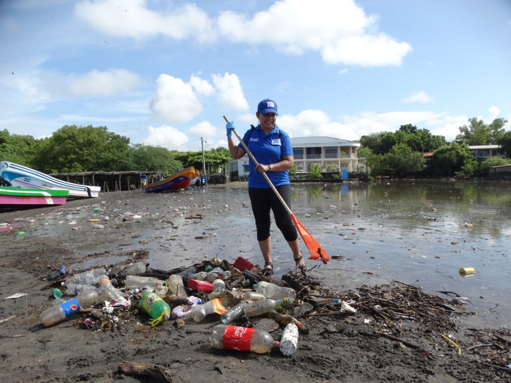 Paso Pacifico coordinator Julie Martinez stands at the seashore raking plastic waste into a pile, 2017. Photo by SetNet Communications.