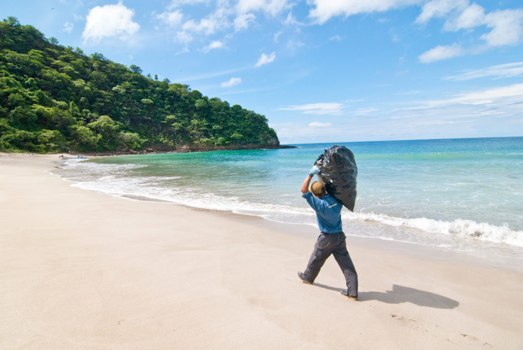 A Paso Pacífico ranger carries a filled black garbage bag across a pristine tropical beach in Nicaragua. Photo by Matt Dolkas.