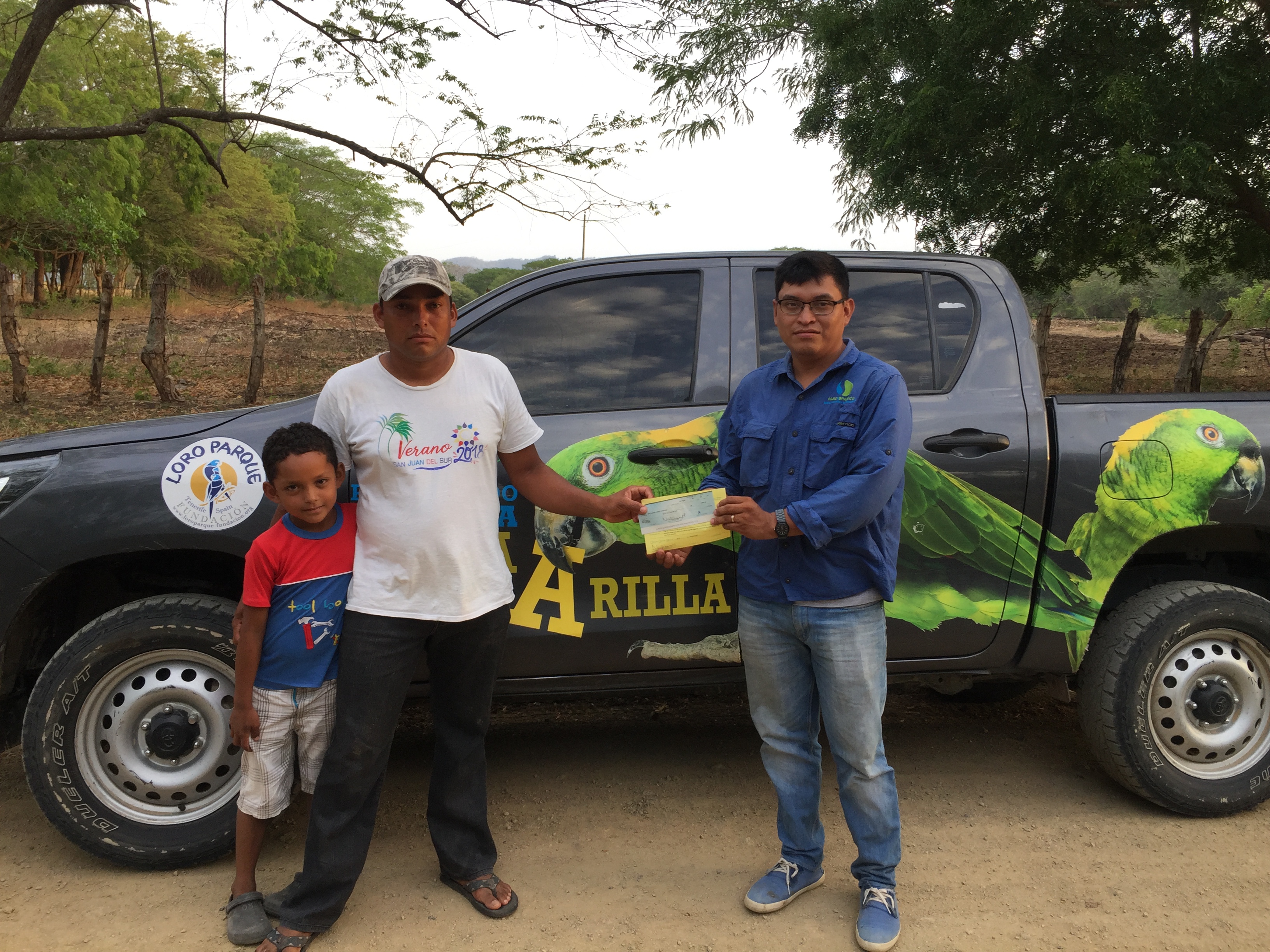 Marcos Calero entrega incentivos a una familia de protectores de loros frente al camión adornado con loros financiado por Loro Parque Fundación.